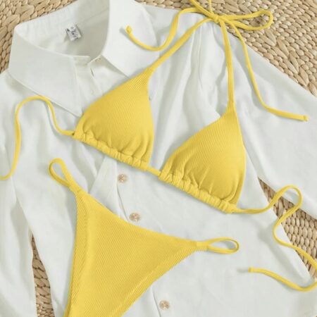 Yellow ribbed triangle bikini placed on a white shirt on top a woven place mat, showcasing textured fabric and beach-inspired styling.